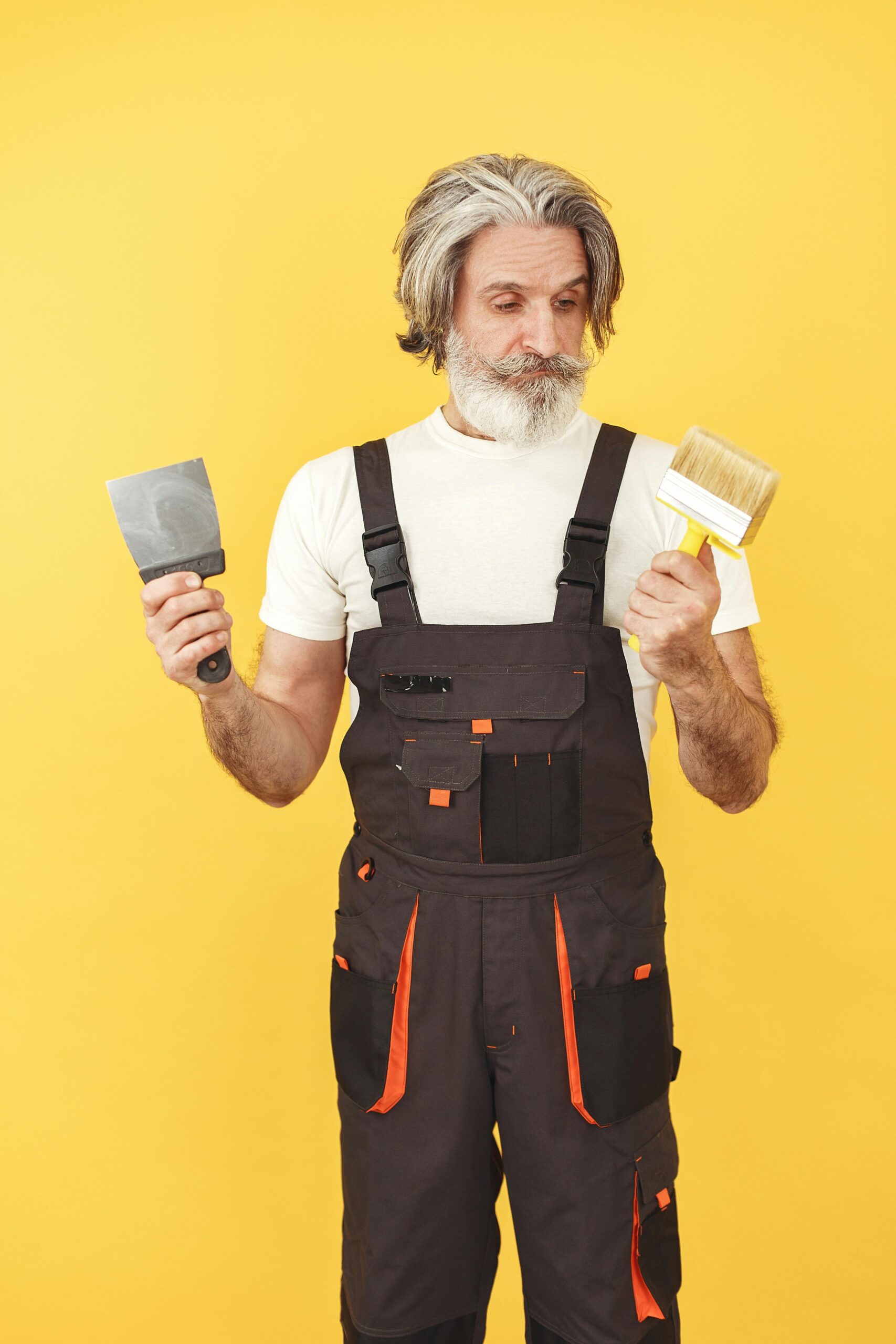 Adult male artisan holding a paintbrush and spatula against yellow background, embodying craftsmanship.